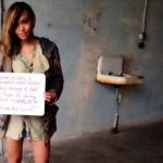 Photo of Jackie Ramos holding a hand-written sign at the Unseen Project at Alcatraz