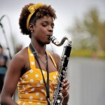 Photo of female saxophone player wearing yellow polka dot dress. 