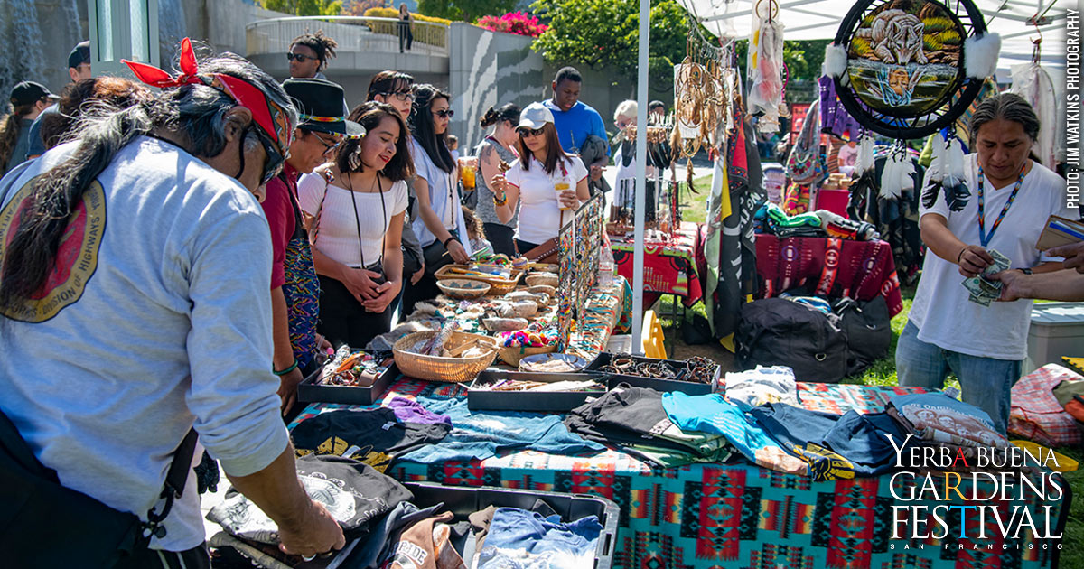 Photo of people gathered around an outdoor table of various crafts by Indigenous Peoples. Photo by Jim Watkins Photography.