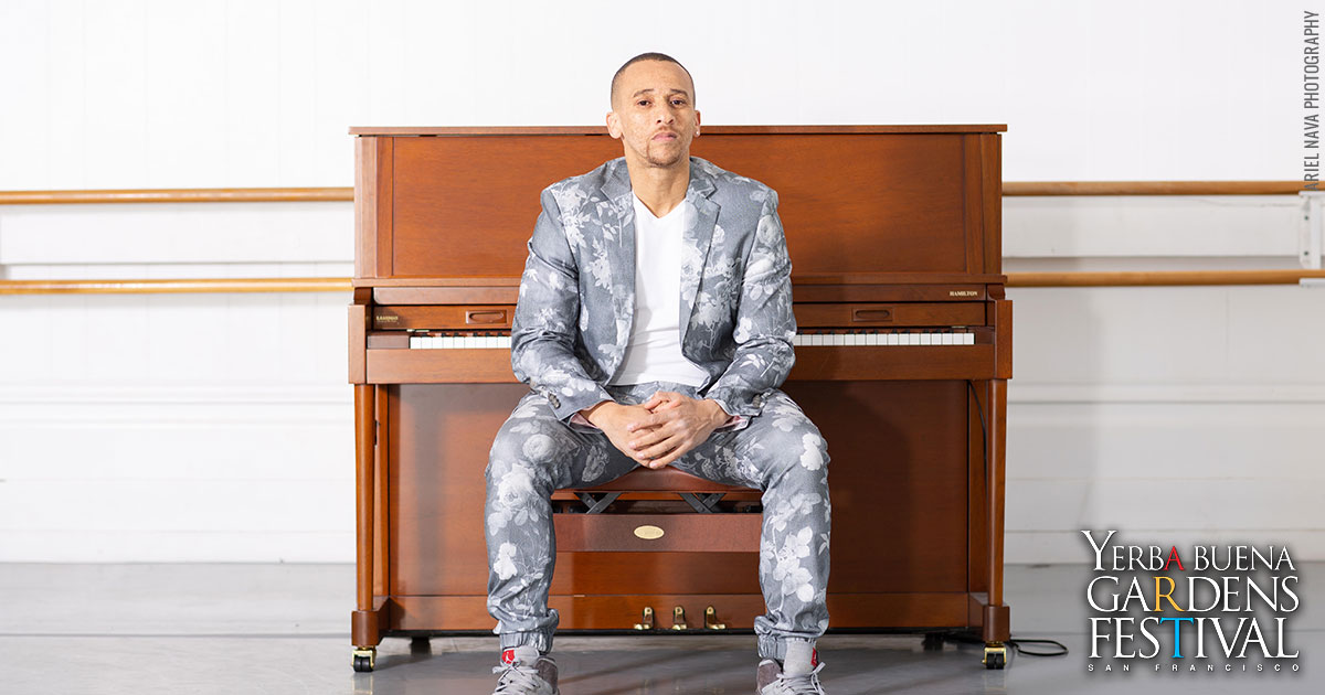 Photo of musician Kev Choice sitting in front of an upright piano.