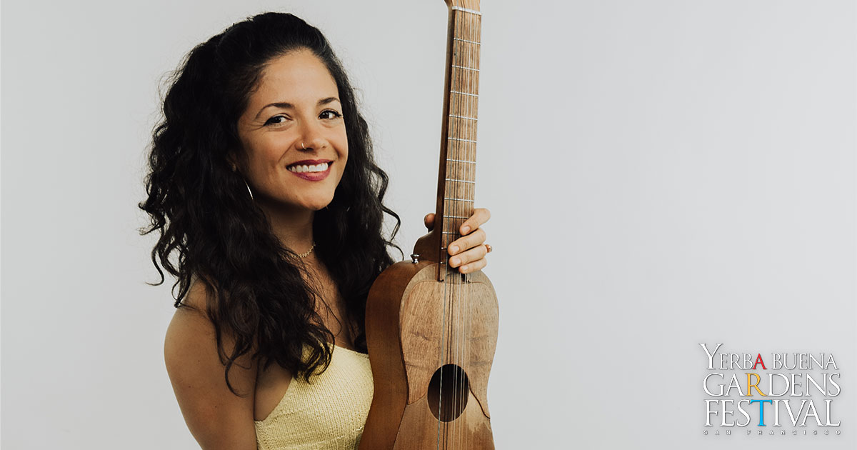 Monica Maria smiling, holding a guitar to her side with one hand