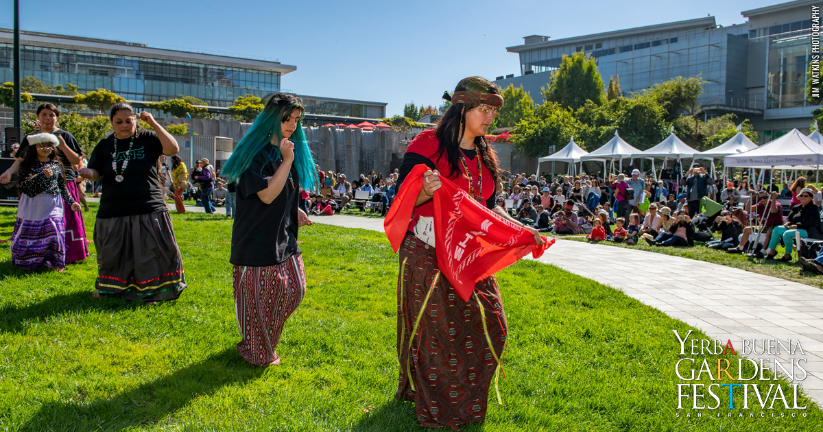 Women of Round Valley Pomo tribe in traditional clothing, dancing on the Yerba Gardens lawn, with an audience watching behind them.
