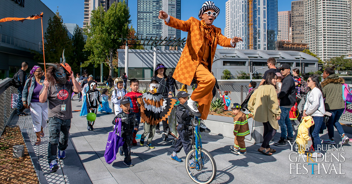 Unique Derique riding a high tricycle, leading the annual Halloween Hoopla Costume parade with dozens of costumed kids and their adults behind him.