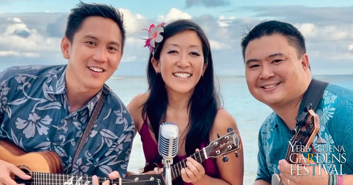 Abe Lagrimas Jr., Cynthia Lin and Ukulenny, smiling in front of a microphone, all holding their own ukuleles, sunny an tropical skies behind them.