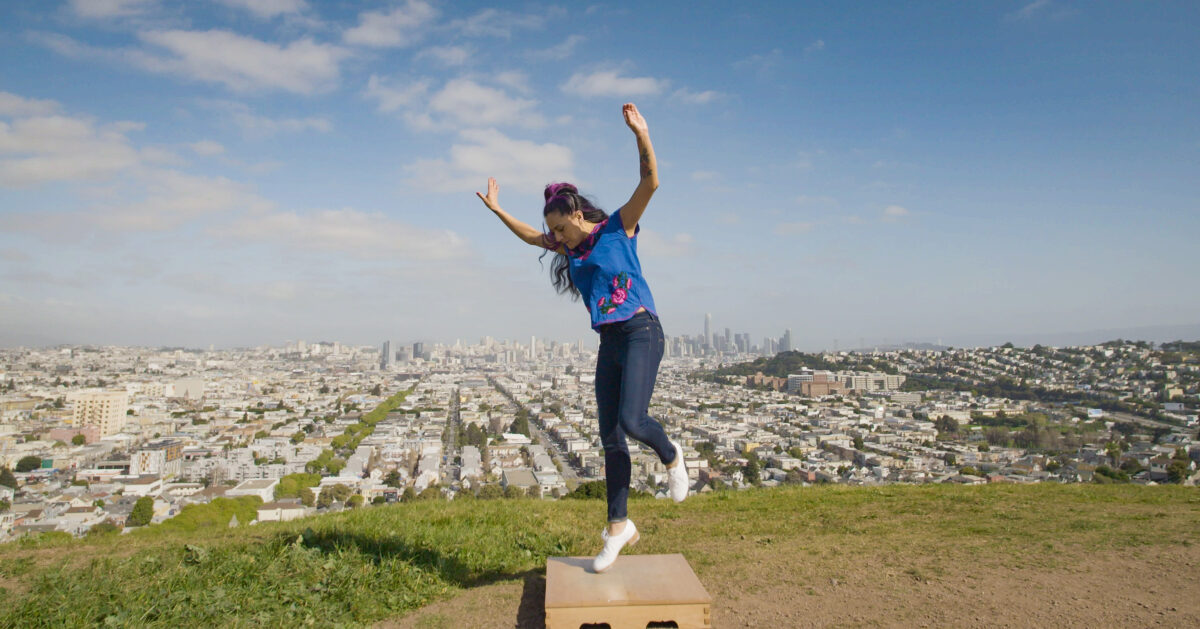 La Mezcla Founding Artistic Director Vanessa Sanchez dancing on a flat top on a high hill with a view of San Francisco behind her.