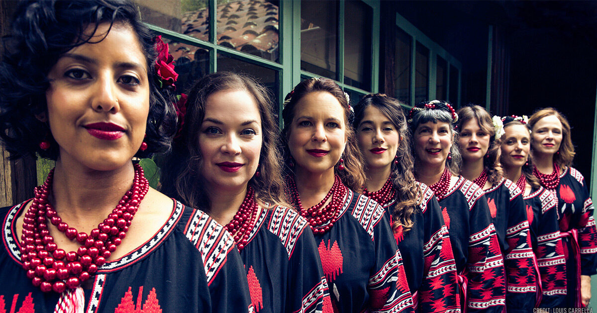 Women of Kitka all wearing red and black outfits, lined up and looking at the camera