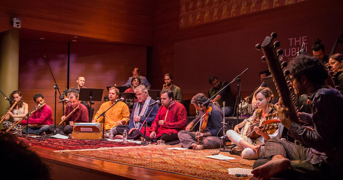 Members of Brooklyn Raga Massive sitting and playing music on a stage floor
