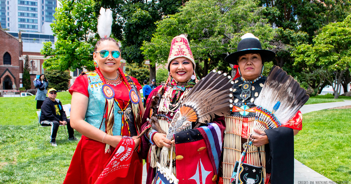 Native women dressed in traditional Indigenous regalia, smiling and standing in Yerba Buena Gardens