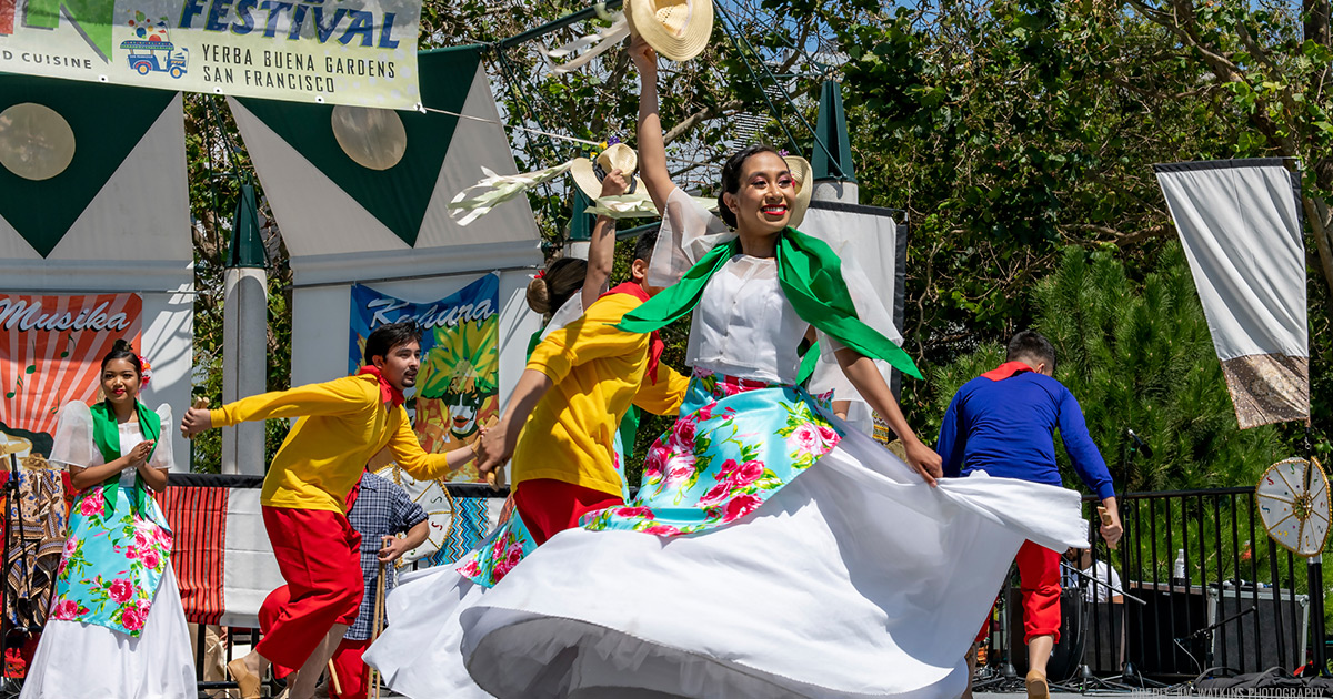 People dressed in colonial wardrobe performing Filipino folk dances and smiling on the Yerba Buena Gardens Festival stage.
