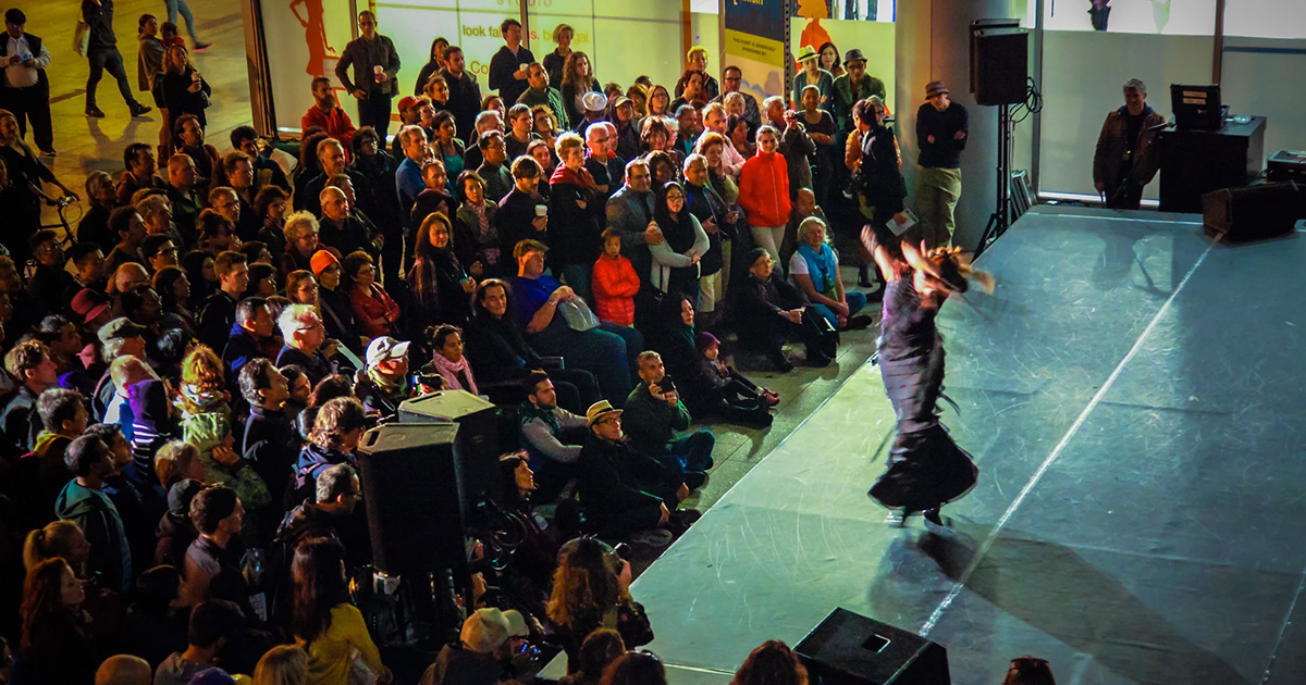 Aerial view photo a dancer performing on an outdoor stage at night, surrounded by a full audience watching.