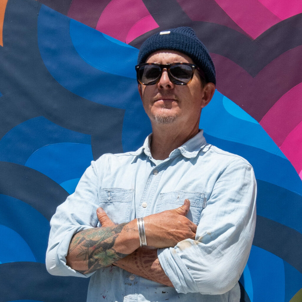 headshot photo of Jet Martinez, arms crossed, in front of the colorful stage banner mural. 