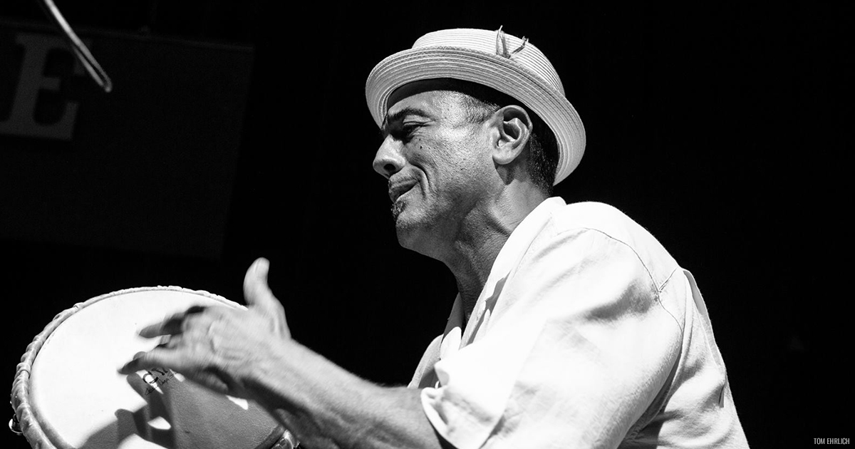 John Santos playing a conga drum in a black and white photo