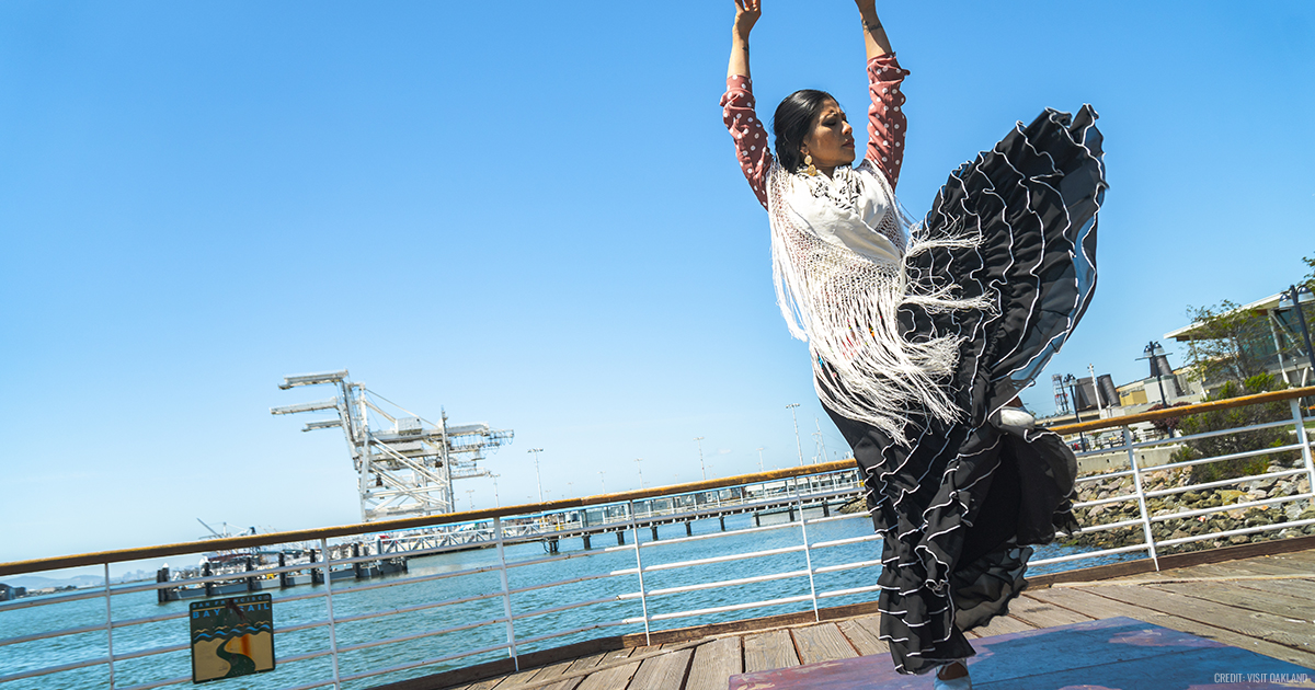 Melissa Cruz in a flamenco dance pose, dress skirt lifted in the wind, on the pier of the Oakland bay.