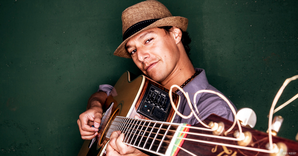 Rafael Bustamante Sarria wearing a fedora hat and holding an acoustic guitar close to his chest