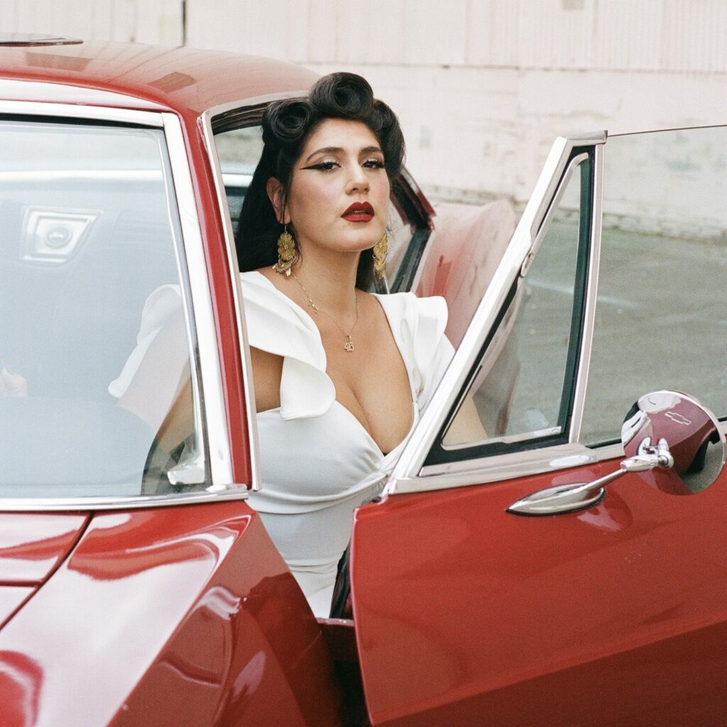 La Doña looking out the door of a red vintage car.