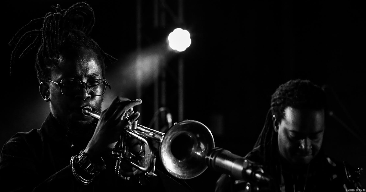Black and white photo of Ndabo Zulu playing trumpet and Linda Sikhakhane playing saxophone behind him