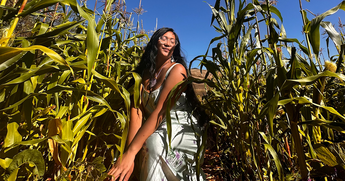 Amihan wearing a light-blue dress, standing amongst a lush green corn crops