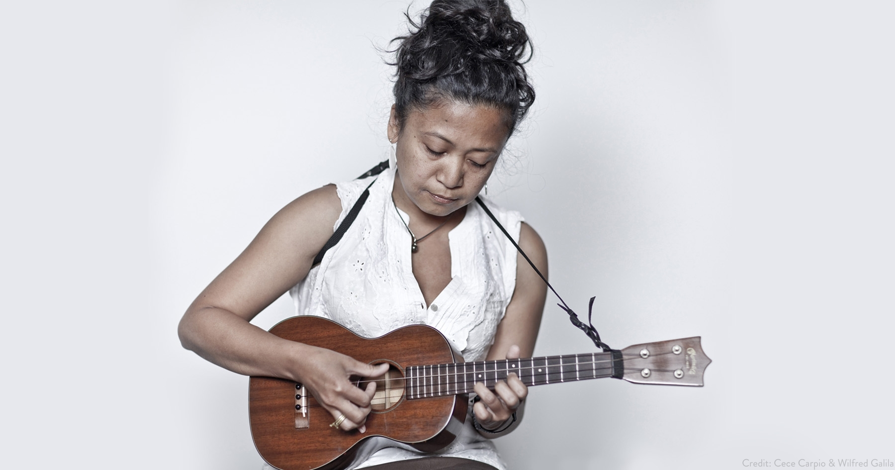 Aireene in a white top looking down at her brown acoustic guitar that she's holding