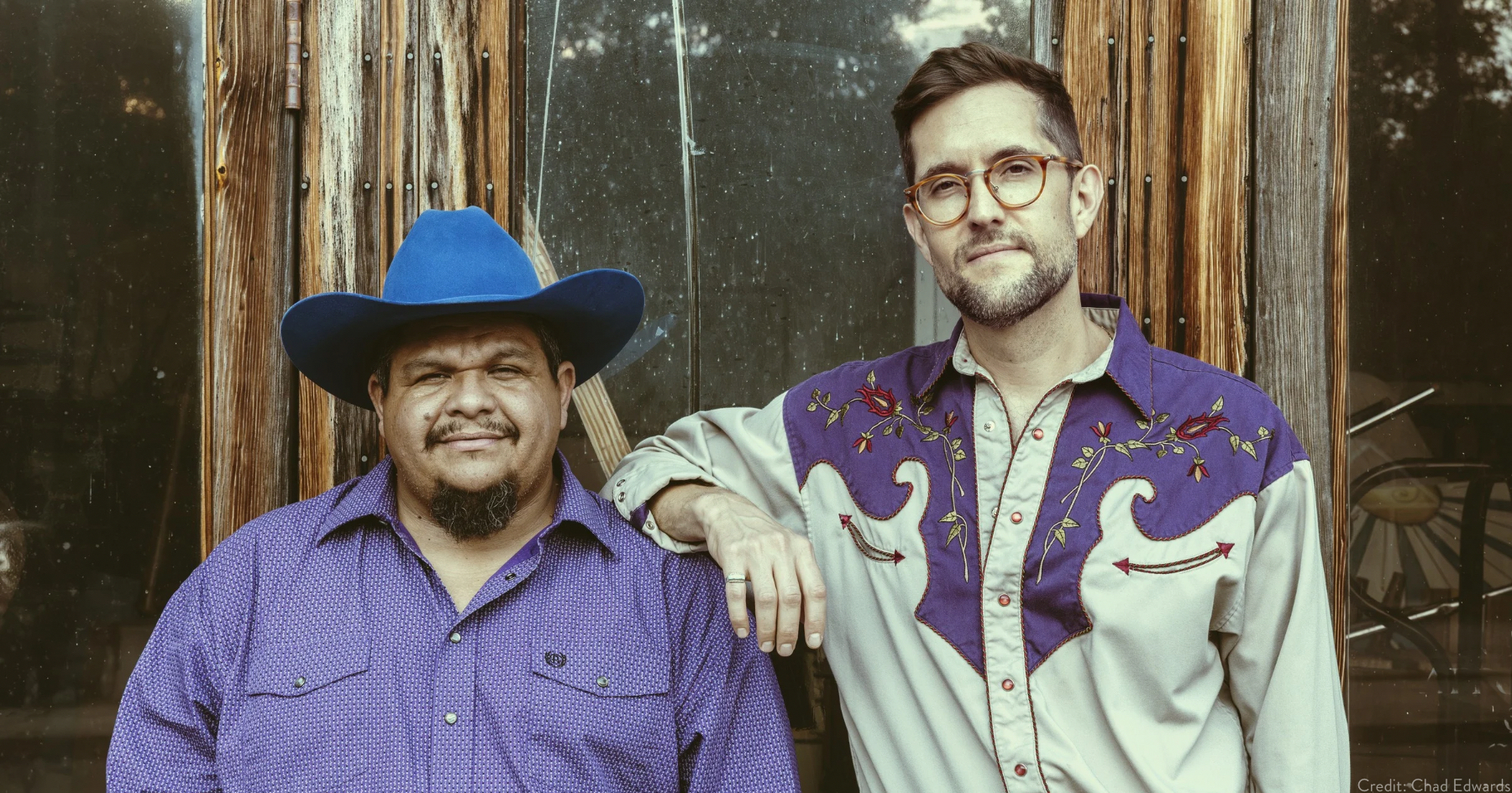Larry (left), in a blue button down shirt and a cowboy hat. Standing beside him is, Joe (right), wearing a white and blue western button down shirt, blue jeans and glasses