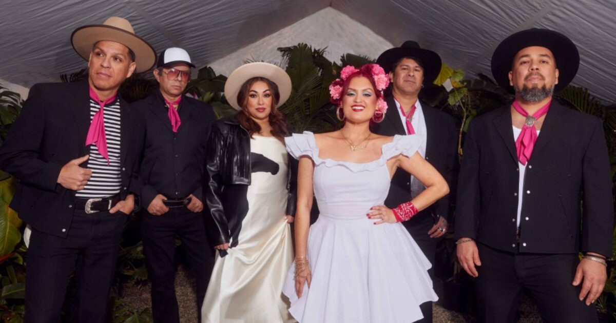 052326_LasCafeteras_1800x945_web Members of Las Cafeteras, wearing black, white and pink outfits, front-facing, standing under a white tent.