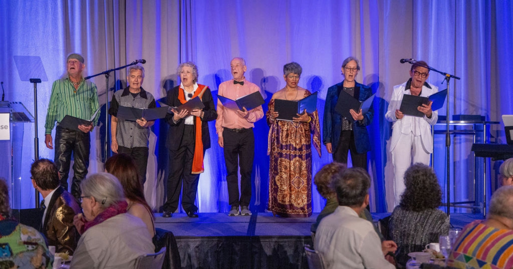 Seven adult choir members performing in front of a seated crowd
