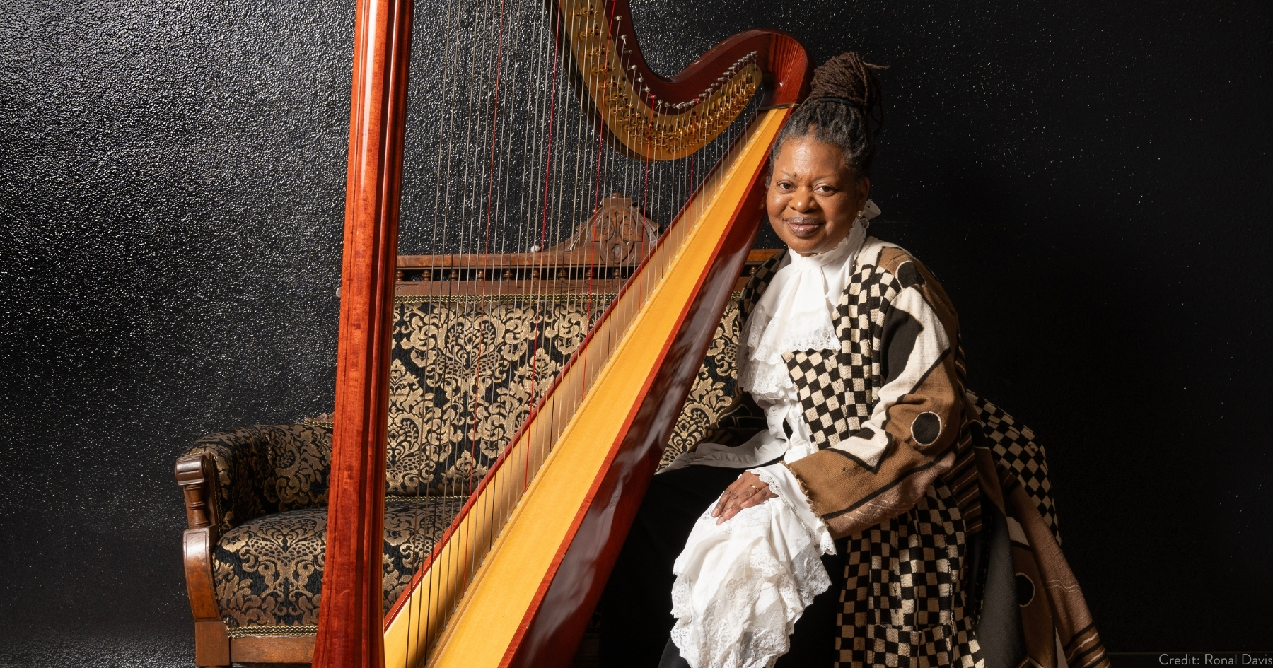 Destiny in a Victorian Era dress, sitting beside her brown floor harp