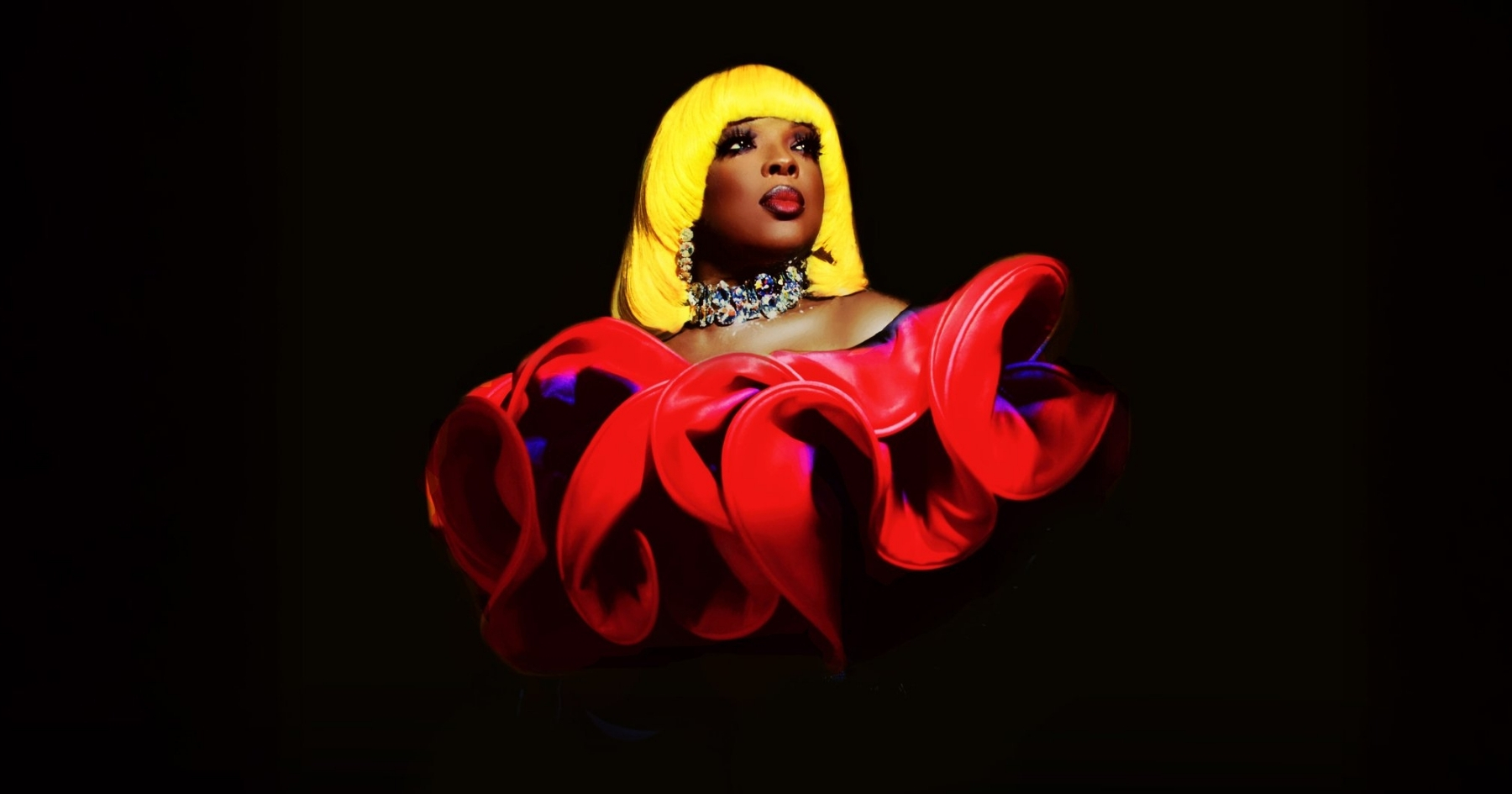Lady Wray with bright yellow hair, wide diamond necklace and ruffled red and black top in front of a black background