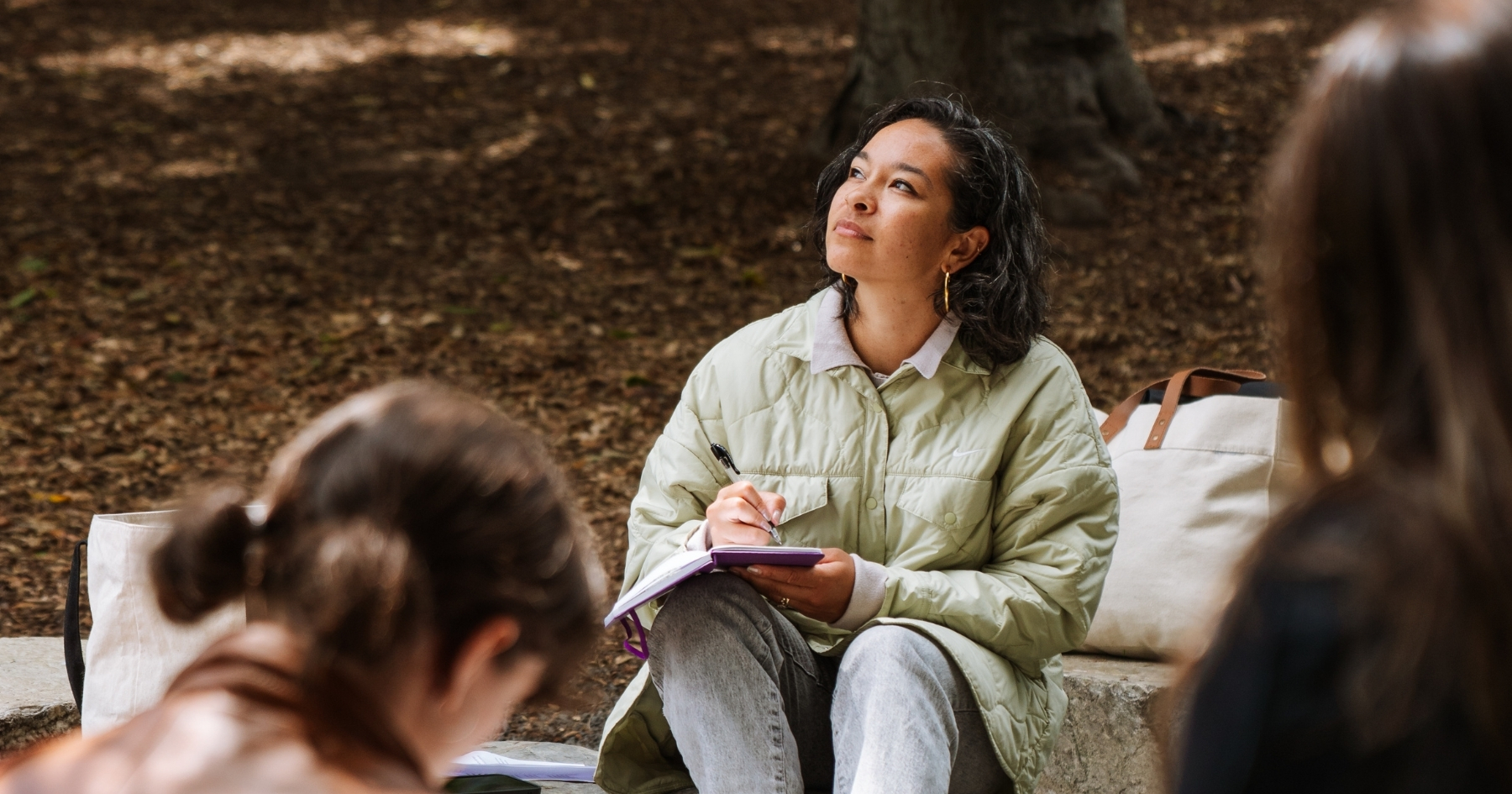 Nia looking up at the sky with her notebook and pen in hand, sitting in front of her students