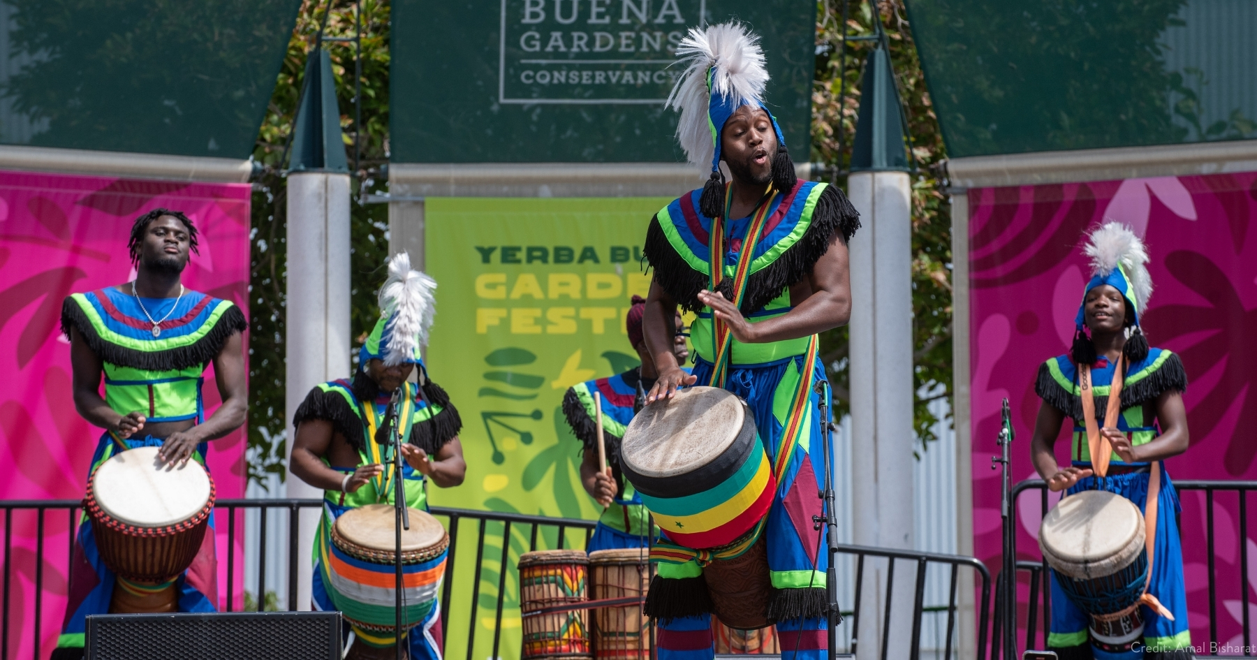Drummers in colorful African regalia, smiling and performing on an outdoor stage