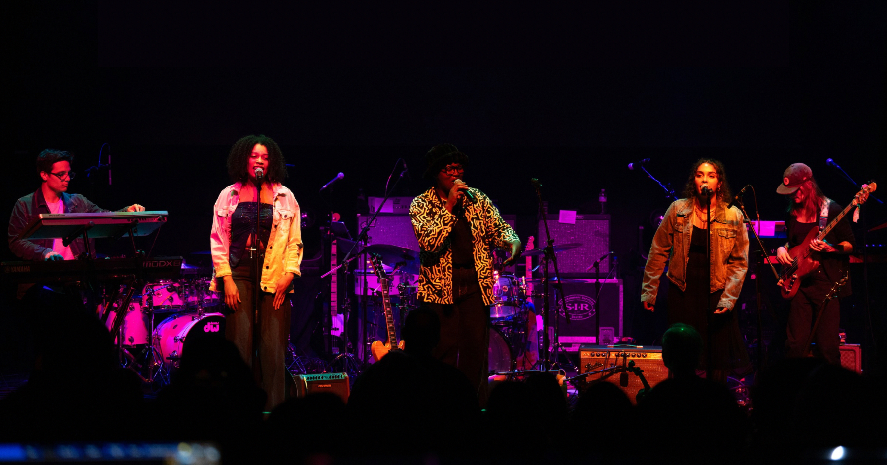 Members of Oakland Rising performing on dark stage under magenta colored lights.