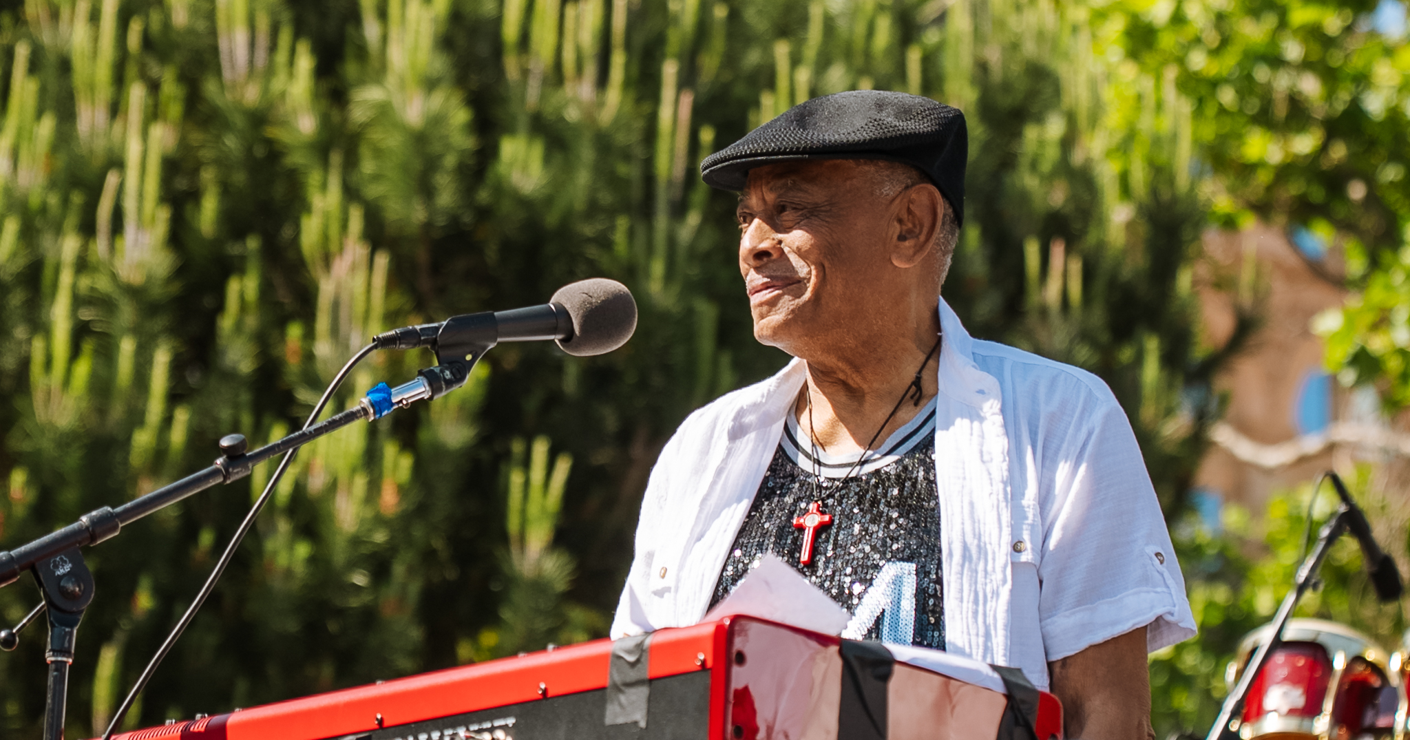 Joe Bataan wearing a black hat and white shirt, smiling